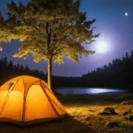 Une tente orange lumineuse installée au bord d'un lac sous un ciel étoilé, avec une lumière douce projetée par une lampe baladeuse à proximité.